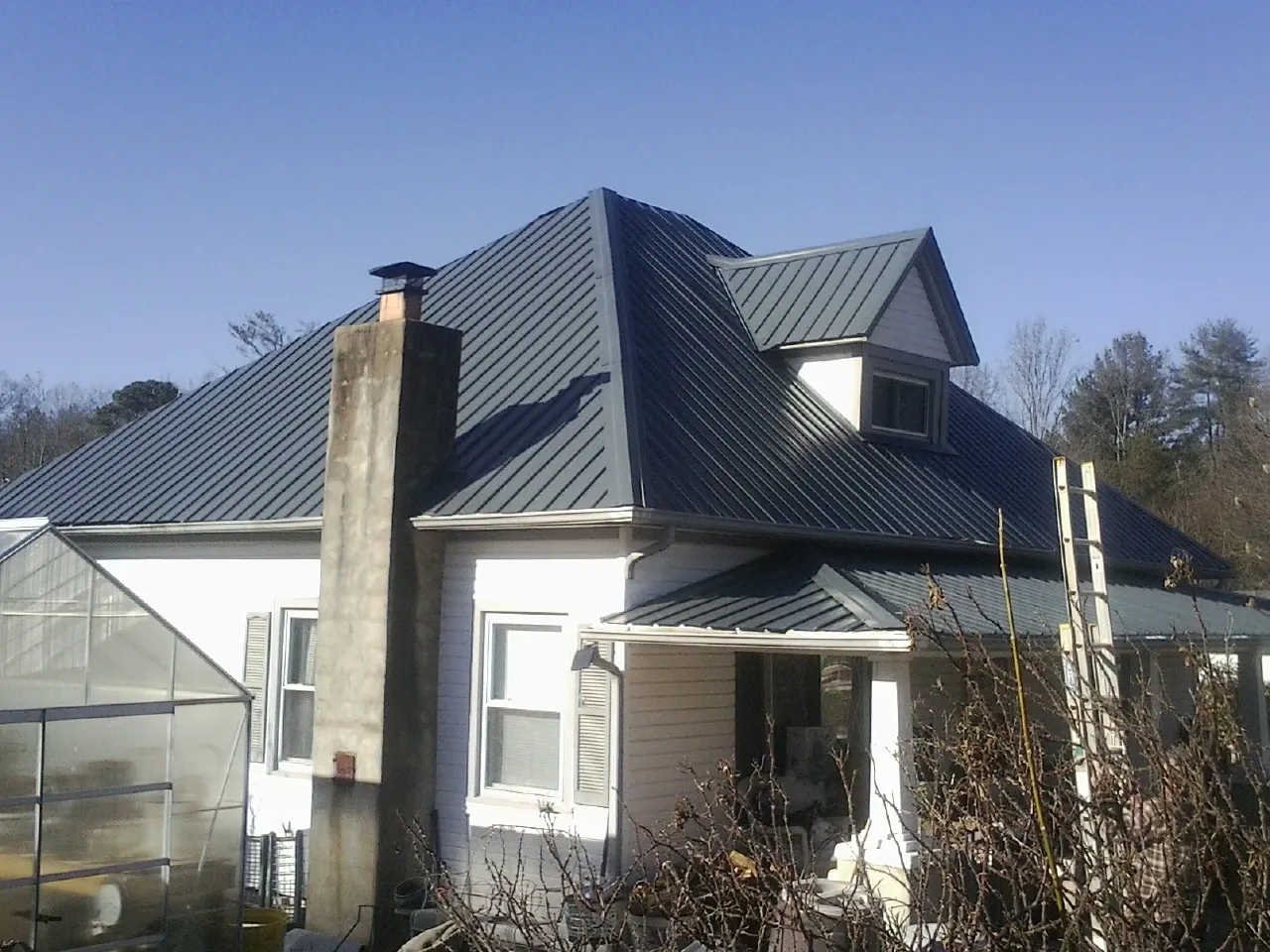 Dark blue standing seam metal roof on a white farmhouse with dormer — Slate & Tile Roof Repair by Roofing Brothers in Woodstock